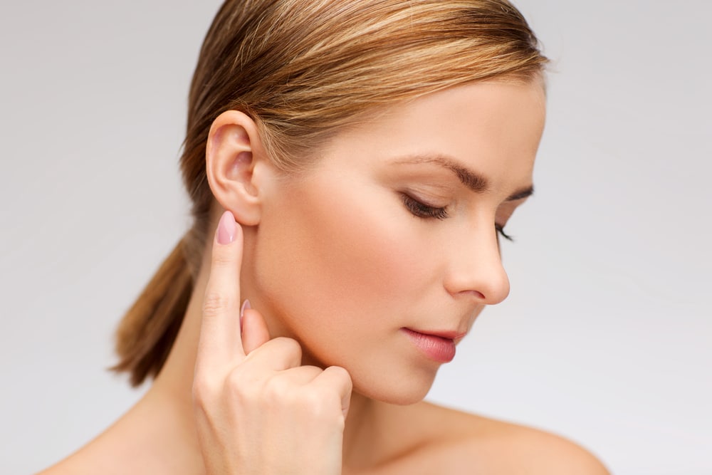 Profile of a woman pointing to her ear after otoplasty ear surgery in Dallas